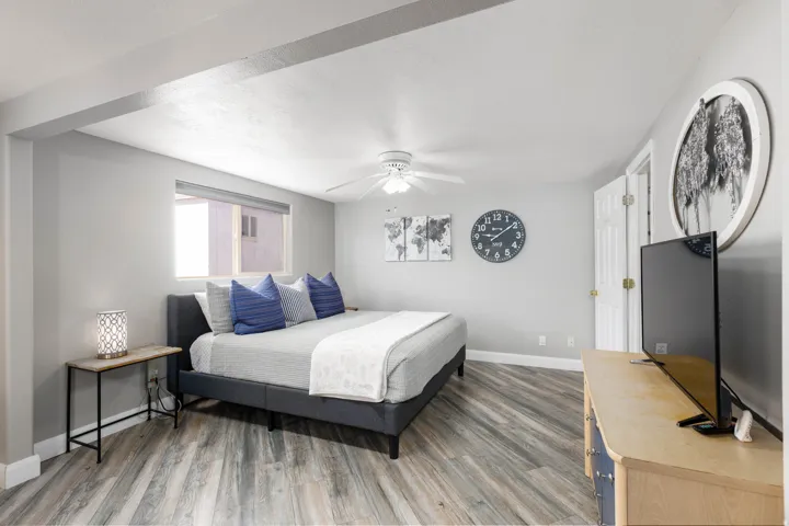 Spacious room with wood-finish flooring, a window with roller shade, and a ceiling fan