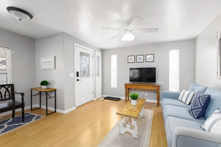 Entryway and living area featuring wood-finish flooring, a white front door with decorative glass, and a ceiling fan with light fixture