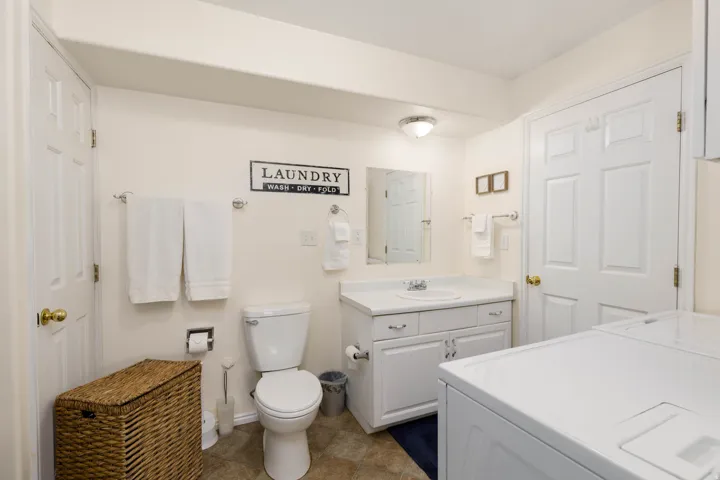 Combination bathroom and laundry area featuring a white vanity with integrated sink, a commode, and a built-in laundry appliance