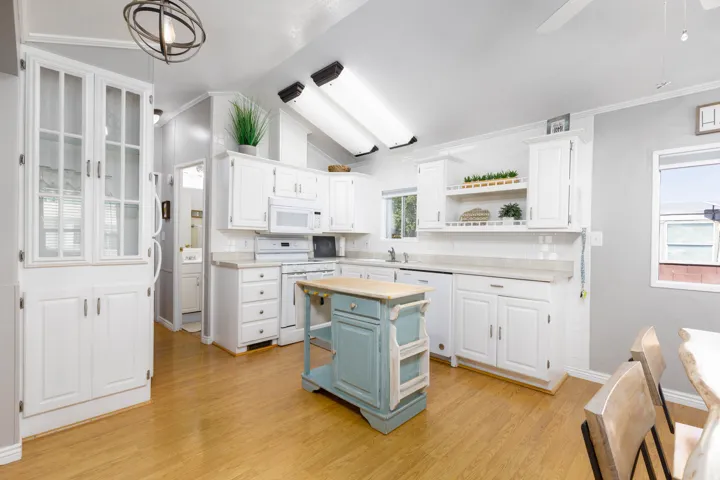 Kitchen featuring white cabinetry, built-in appliances, wood-finish flooring, a vaulted ceiling, and an island with a light-toned countertop