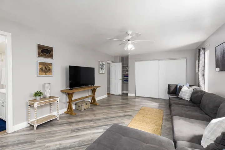 Spacious room featuring wood-finish flooring, light gray walls, a ceiling fan, and white baseboards
