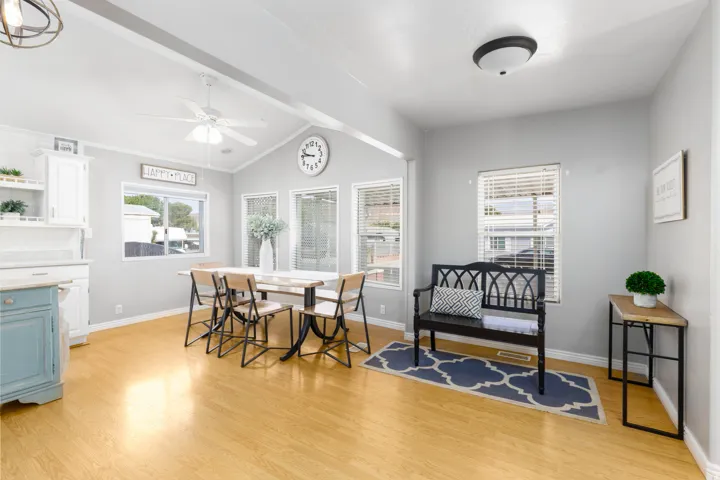 Bright living area featuring wood-finish flooring, vaulted ceilings with exposed beams, and multiple windows with blinds