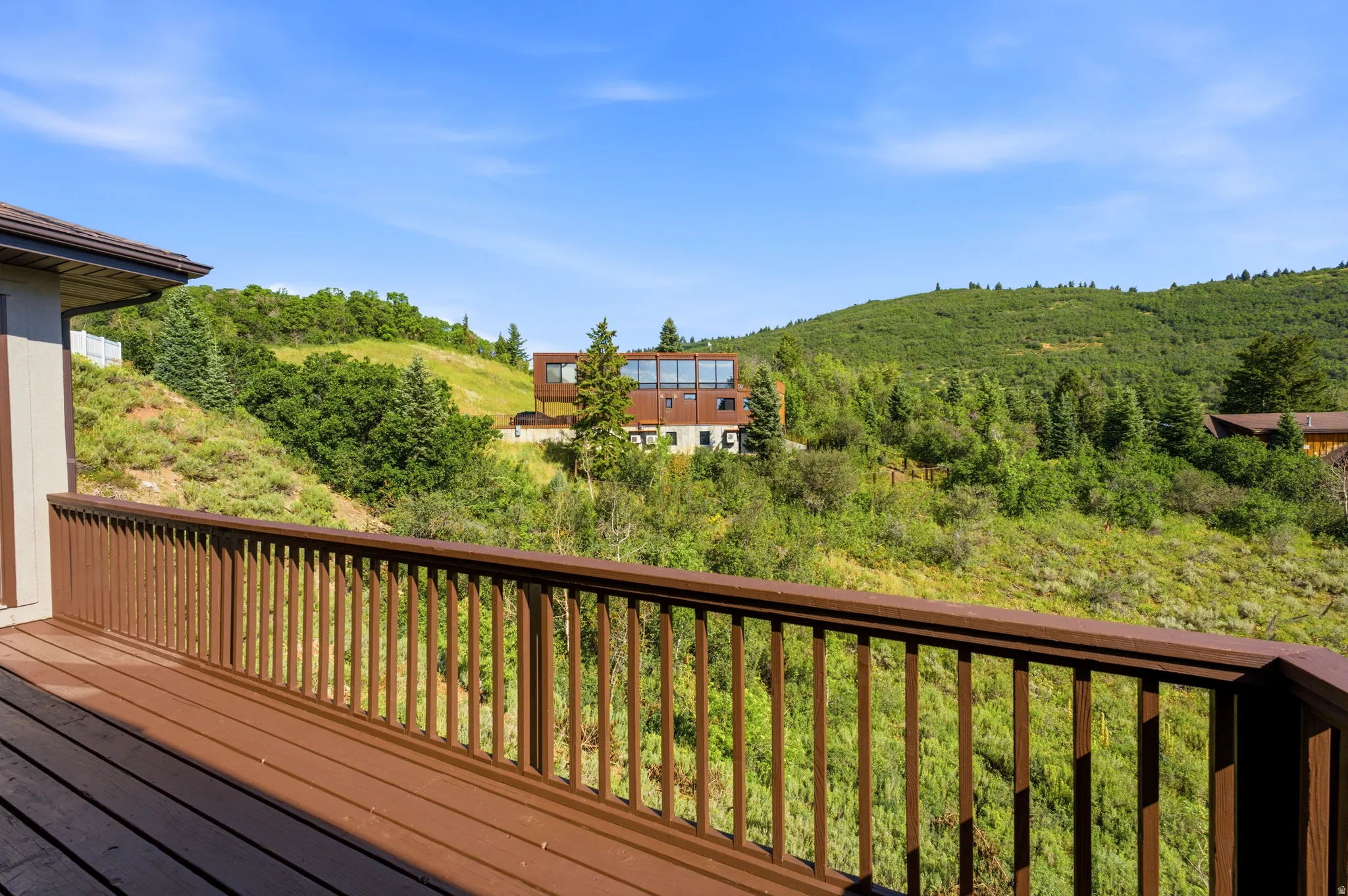 Spacious outdoor deck with brown railing, offering expansive views of rolling green hills and distant properties