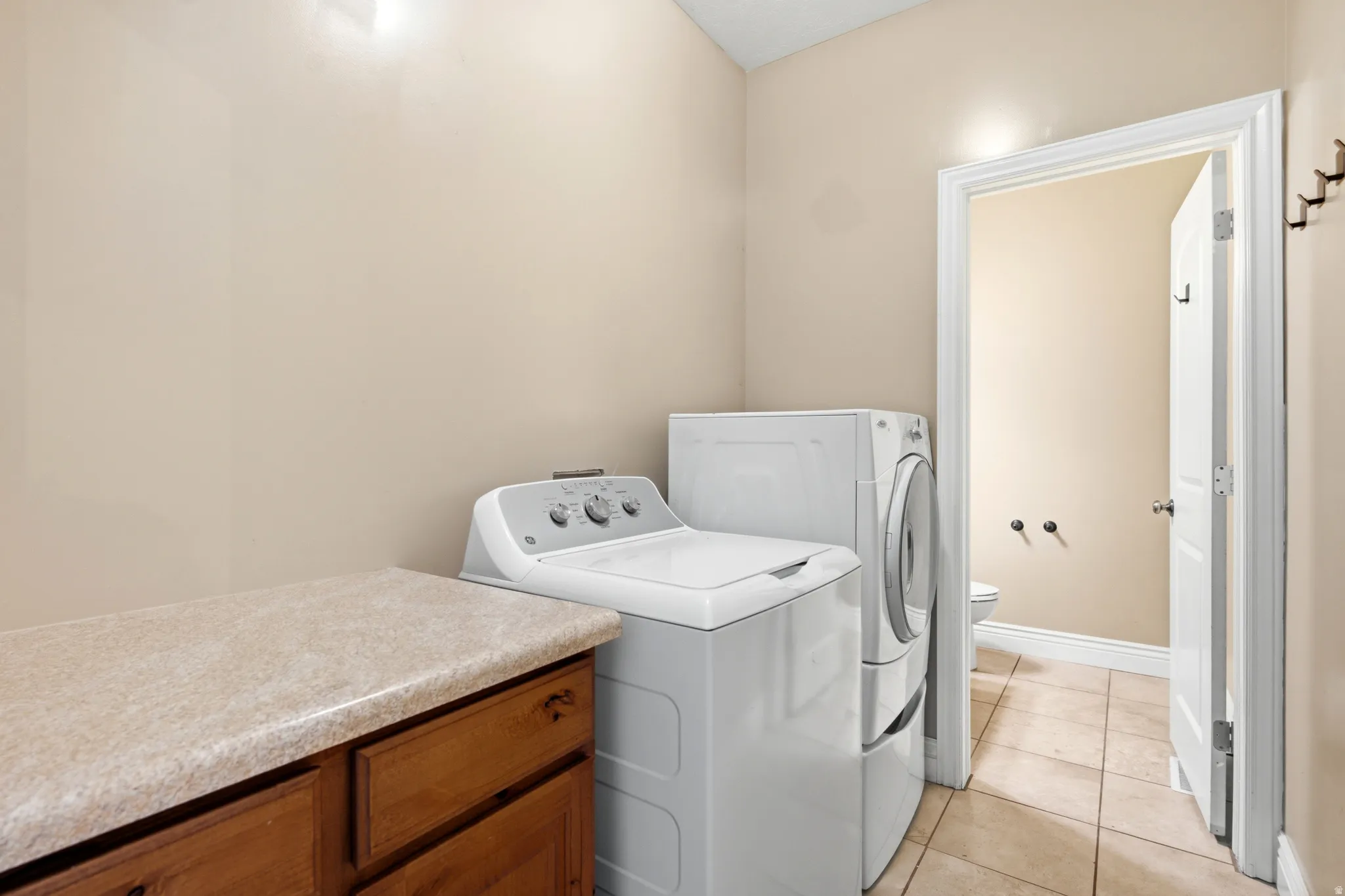 Dedicated laundry area featuring a built-in wood-finish cabinet with a light-toned countertop, and tile flooring