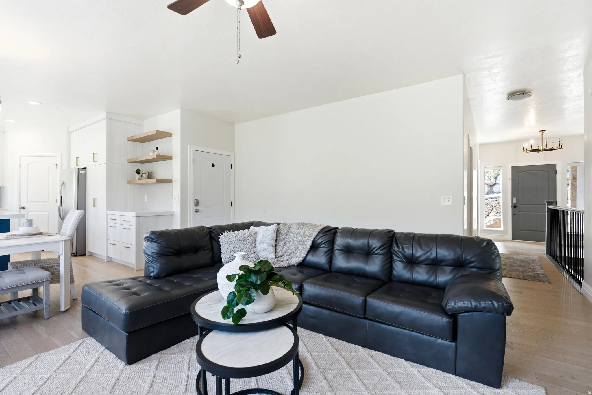Open-concept living area featuring light wood-finish flooring, white walls, and a ceiling fan