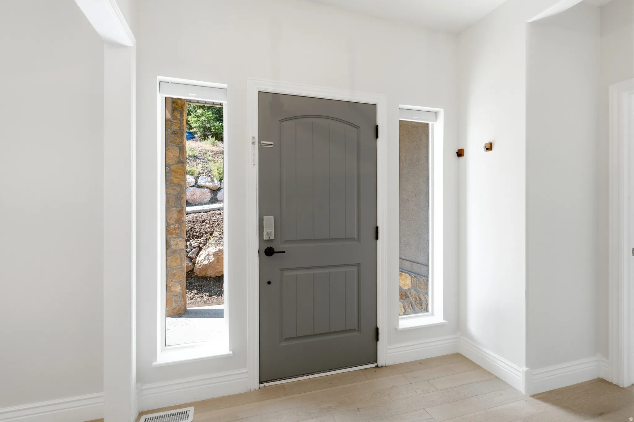 Entryway featuring a paneled door, two vertical sidelight windows, light wood-finish flooring, white baseboards, and white walls