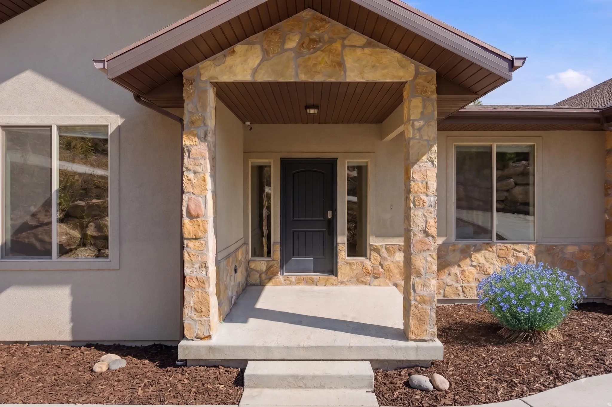 Stucco exterior with stone accents, covered entry, dark paneled entry door, and side-light windows