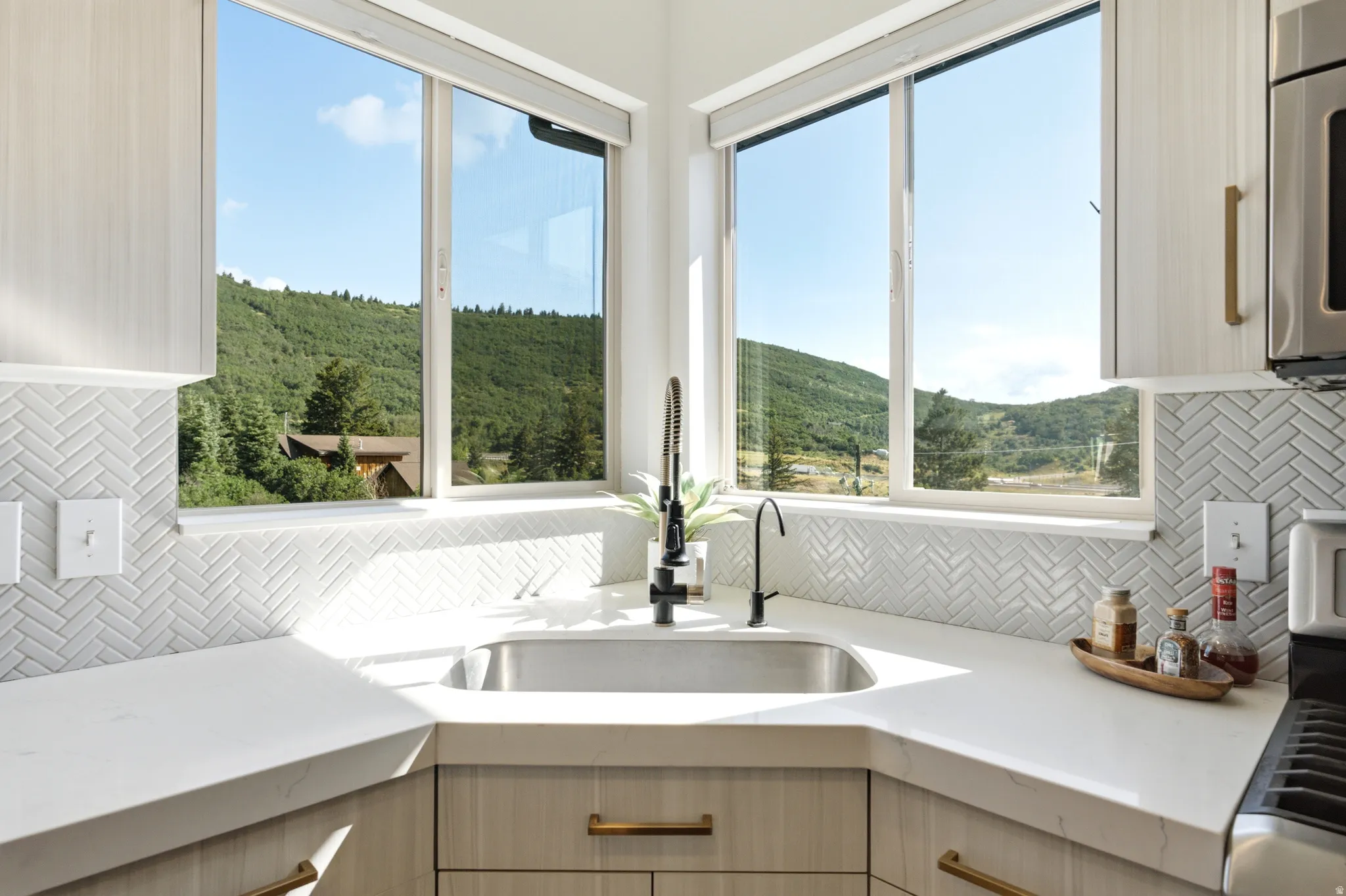 Corner kitchen sink with a stainless steel basin, contemporary black faucet, and white countertops