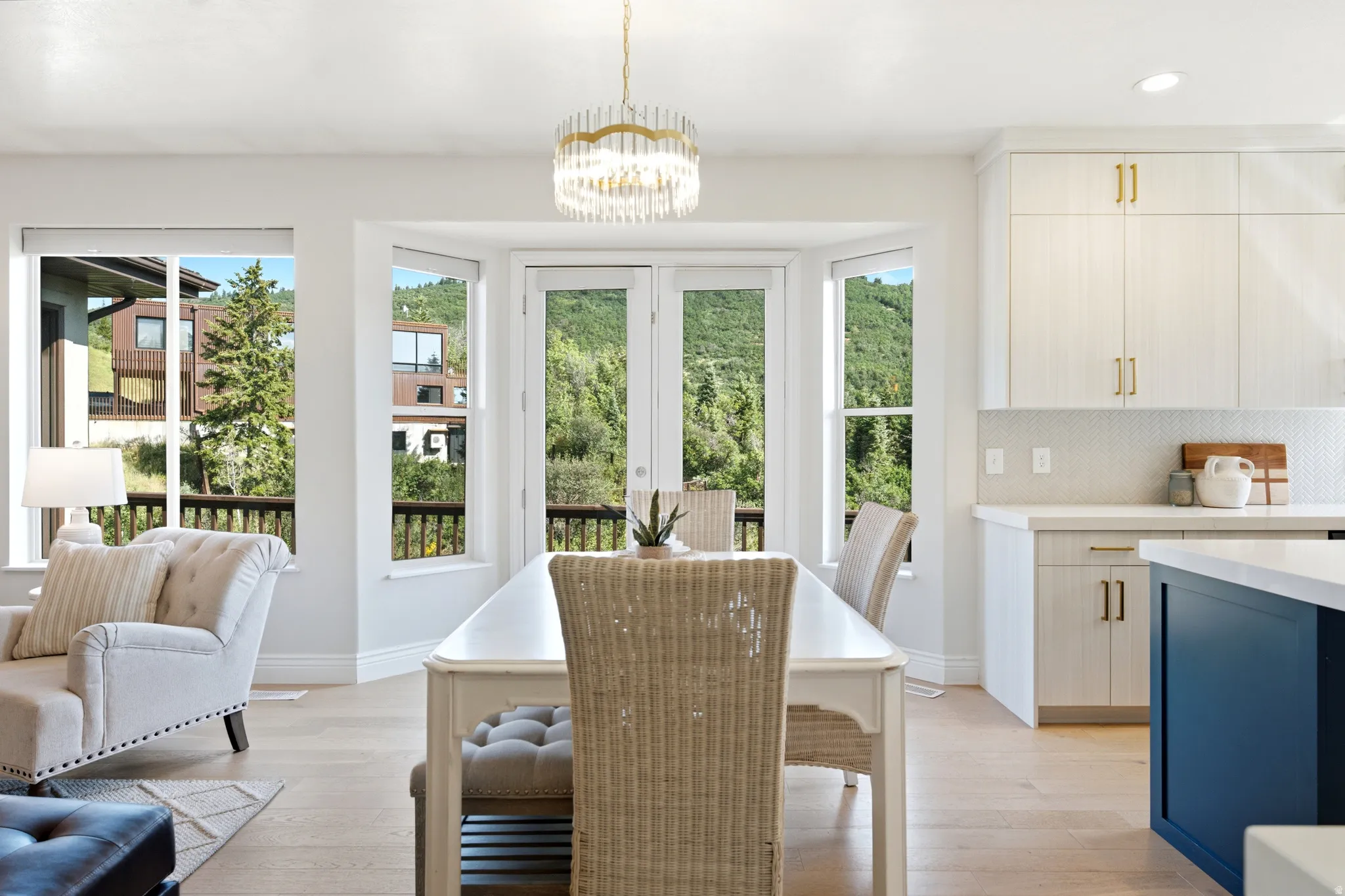 Bright dining area featuring a modern chandelier, light wood-finish flooring, and bay windows with French doors