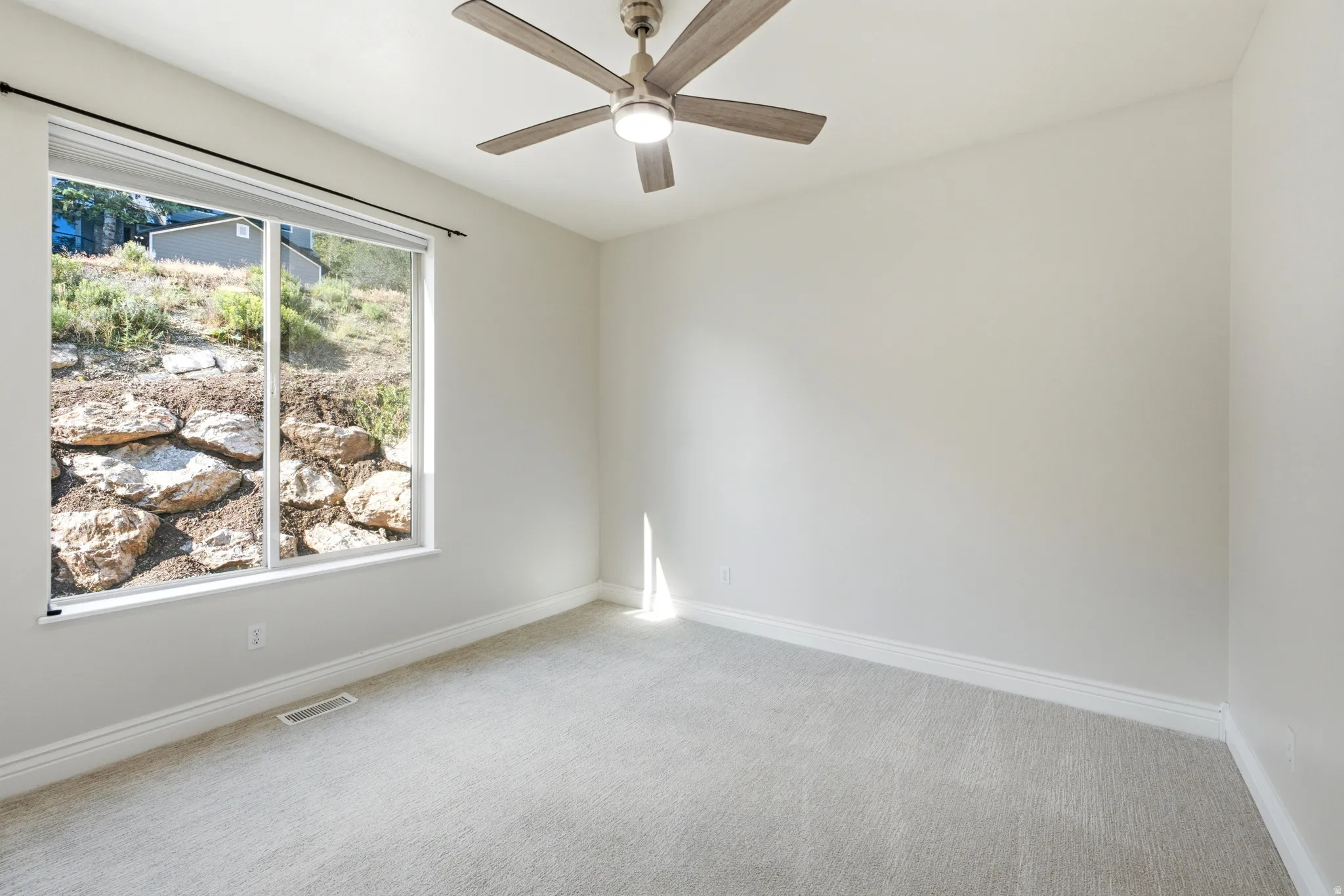 Spacious room featuring light gray carpet flooring, white baseboards, and a neutral wall color