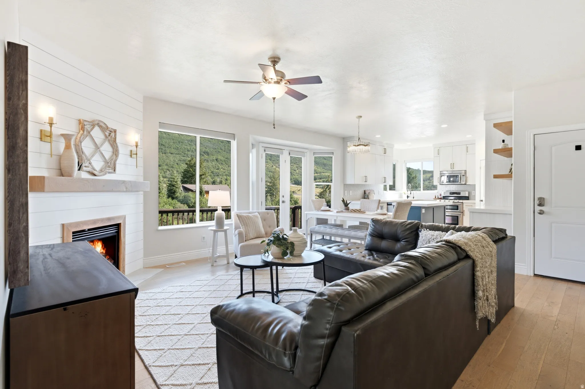 Open-concept living area featuring a shiplap fireplace with wood mantel, large windows, French doors, and wood-finish flooring