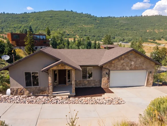 Stone and stucco exterior with an attached garage, covered entryway, and concrete driveway