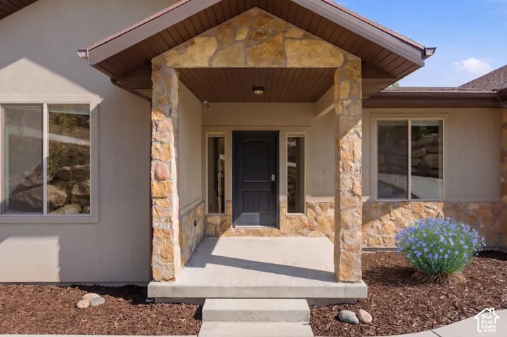 Stucco exterior with stone accents, covered entry, dark paneled entry door, and side-light windows