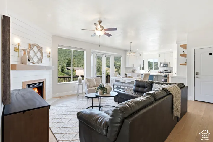 Open-concept living area featuring a shiplap fireplace with wood mantel, large windows, French doors, and wood-finish flooring