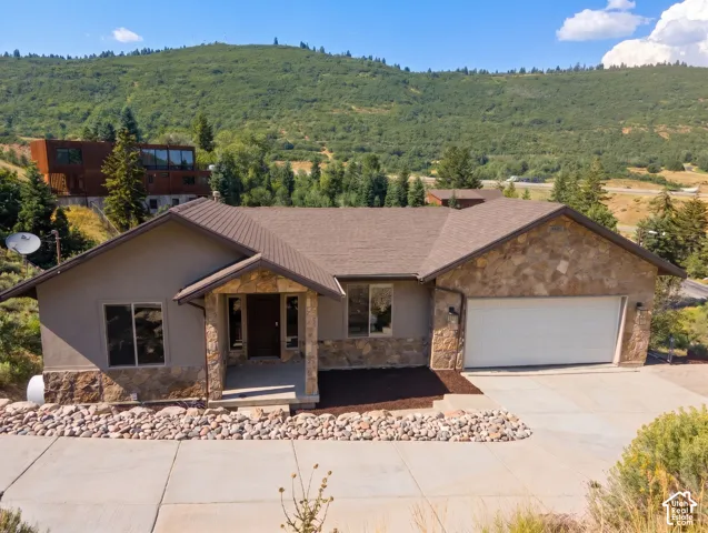 Stone and stucco exterior with an attached garage, covered entryway, and concrete driveway