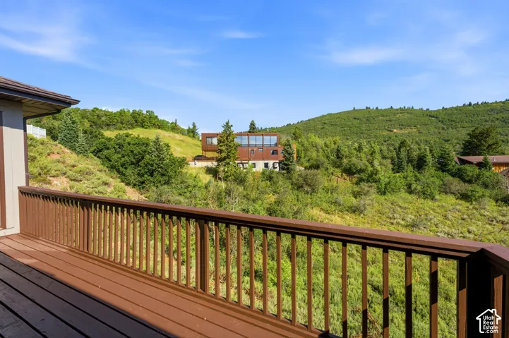 Spacious outdoor deck with brown railing, offering expansive views of rolling green hills and distant properties