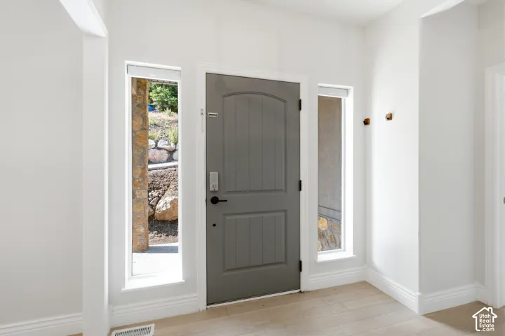 Entryway featuring a paneled door, two vertical sidelight windows, light wood-finish flooring, white baseboards, and white walls