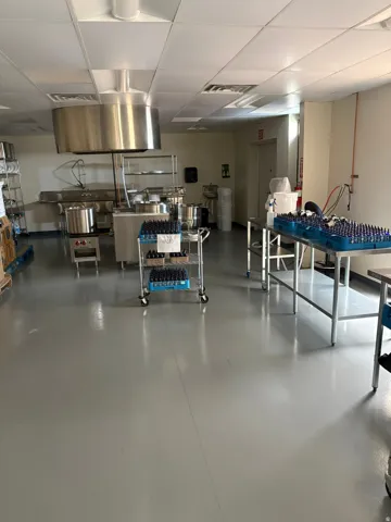 Spacious commercial kitchen featuring a large stainless steel exhaust hood, light gray flooring, and white ceiling tiles