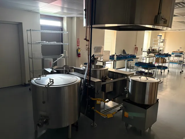 Commercial kitchen space featuring stainless steel equipment, overhead exhaust hood, wire shelving, and extensive counter areas