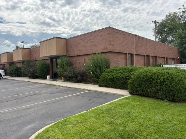 Brick commercial building with multiple entrances, dedicated parking lot, and mature landscaping