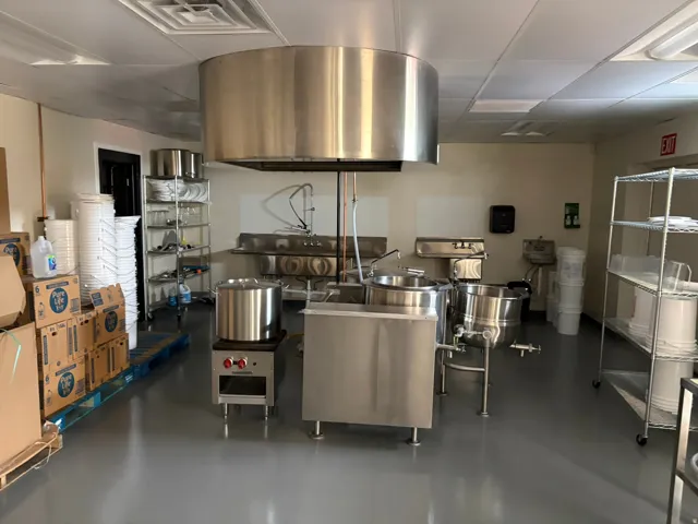 Commercial kitchen space featuring a large central stainless steel exhaust hood, a three-compartment stainless steel sink, and durable gray epoxy flooring
