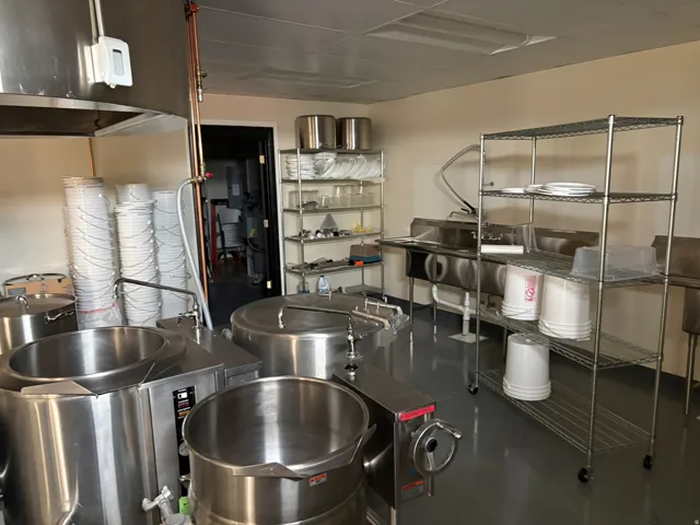 Commercial kitchen featuring stainless steel equipment, industrial-grade flooring, ample shelving, and a triple-basin sink