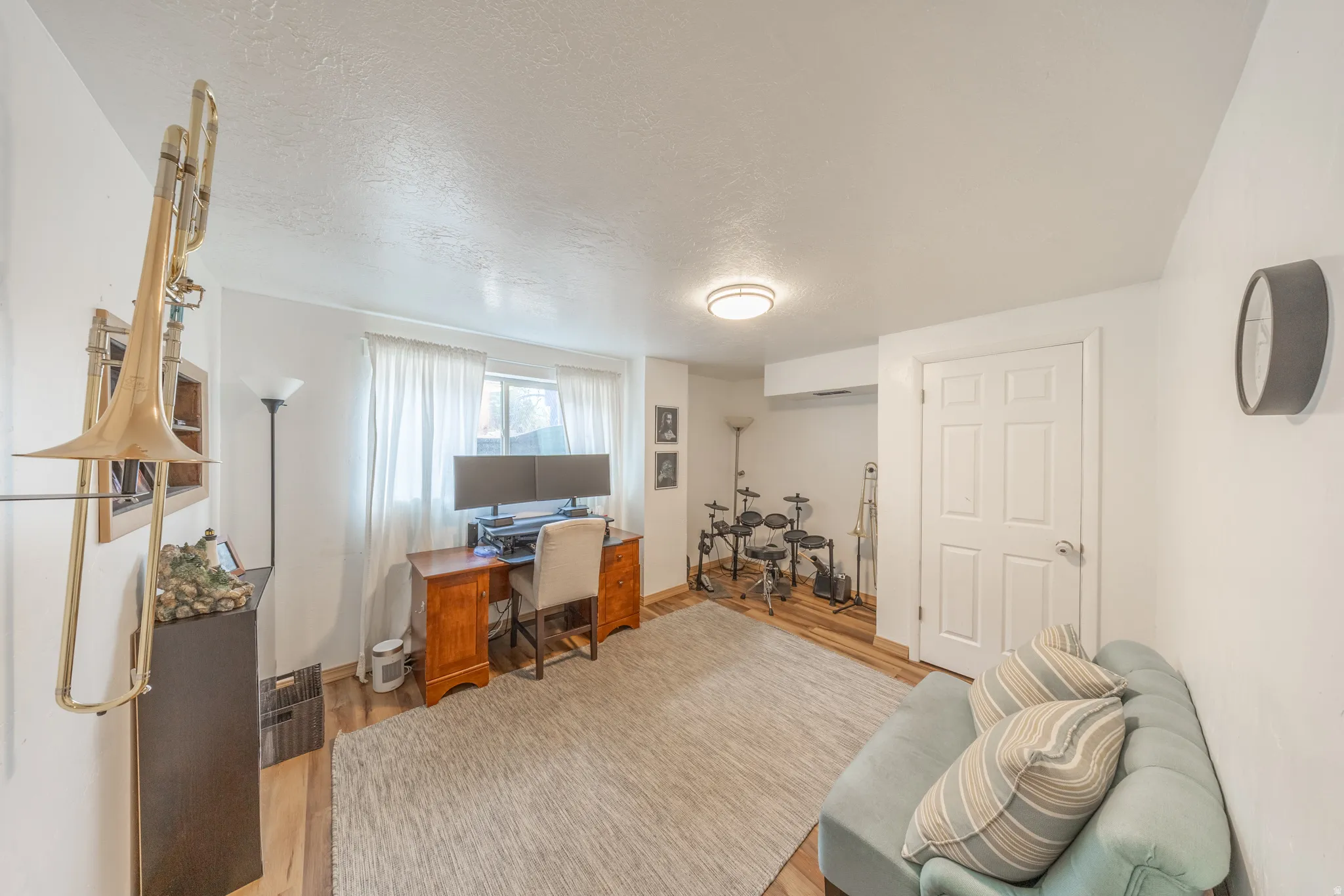 Versatile room featuring wood-finish flooring, a bright window with sheer white curtains, and a flush-mount ceiling light