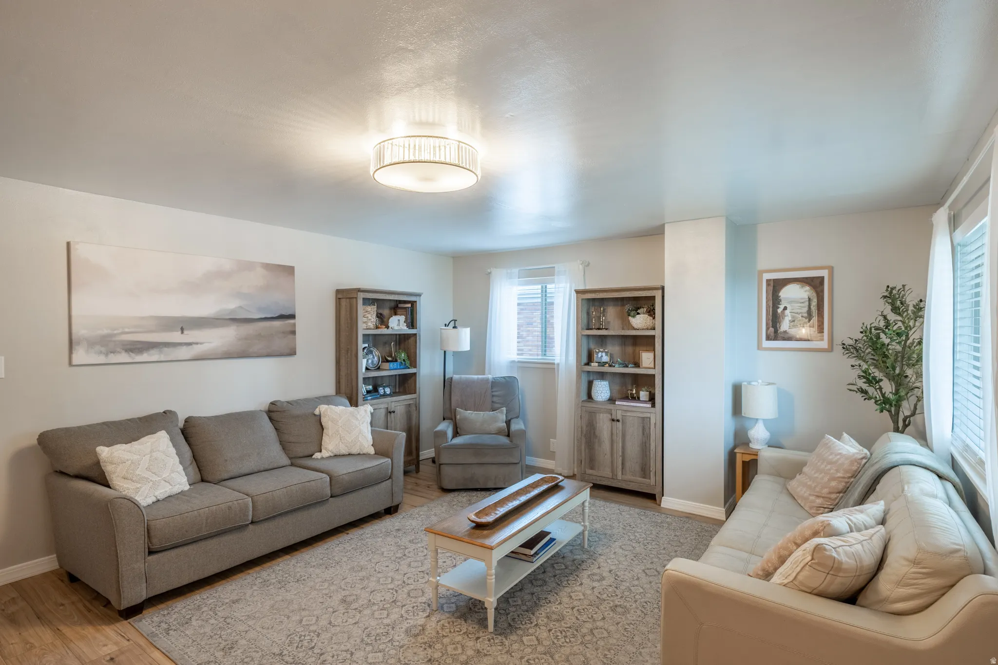 Spacious living area featuring light-toned walls, wood-finish flooring, and a decorative ceiling light fixture