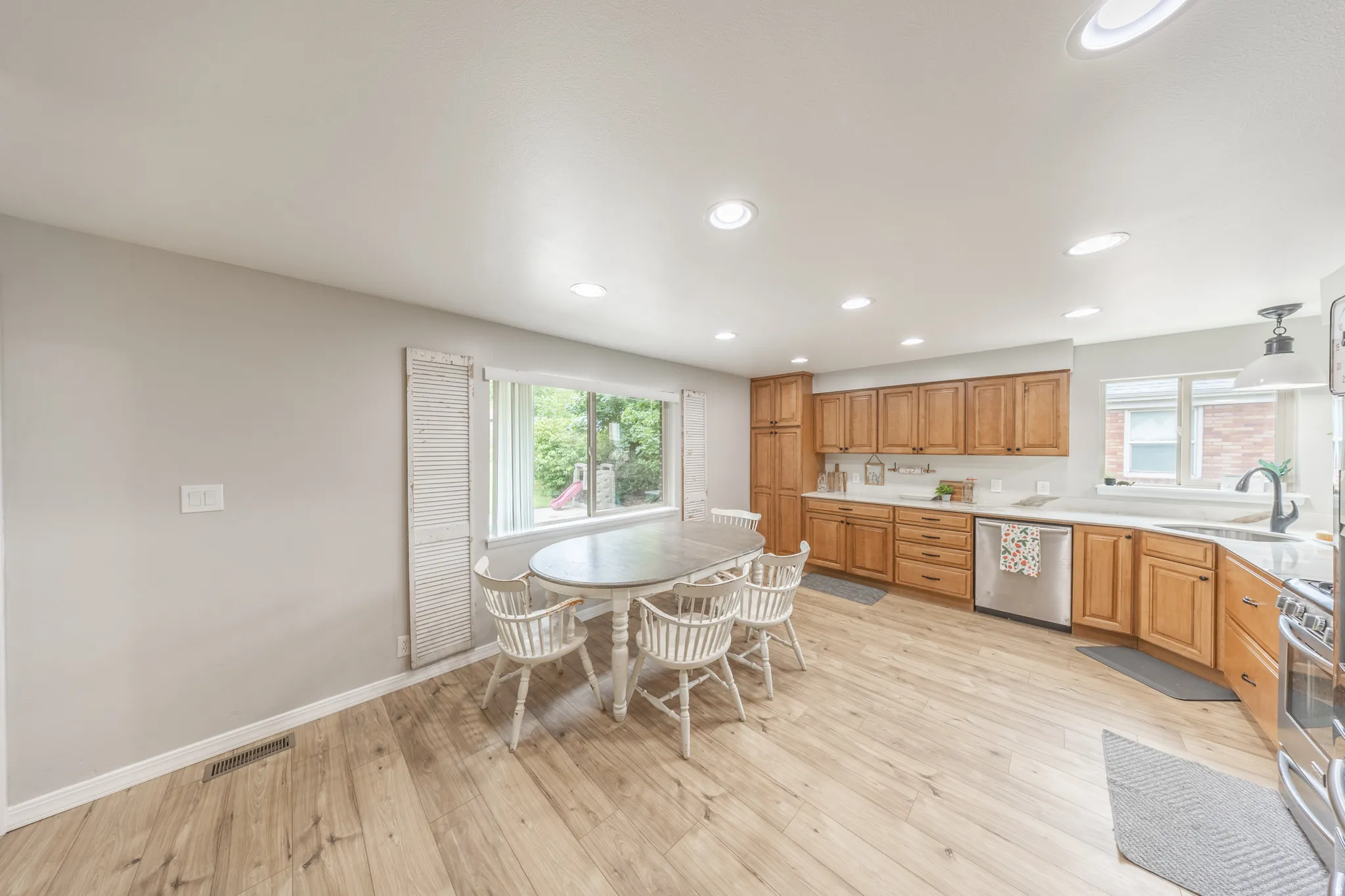 Kitchen and dining area featuring wood-finish flooring, recessed lighting, and a window with white shutters