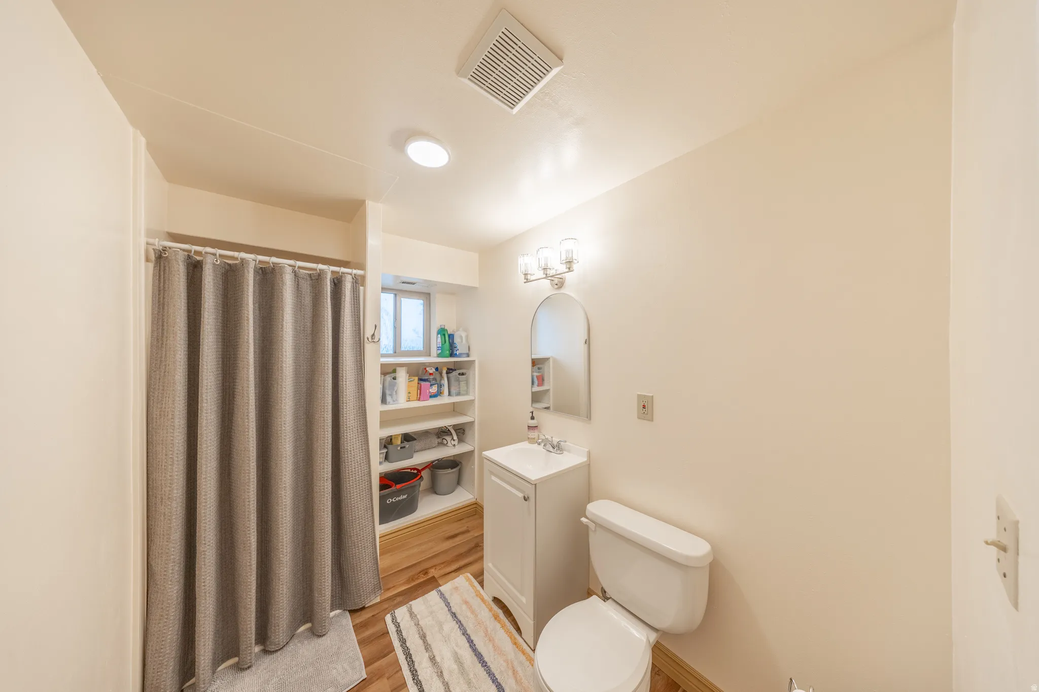 Bathroom with a single vanity, wood-finish flooring, a built-in shelving unit, and a shower enclosure