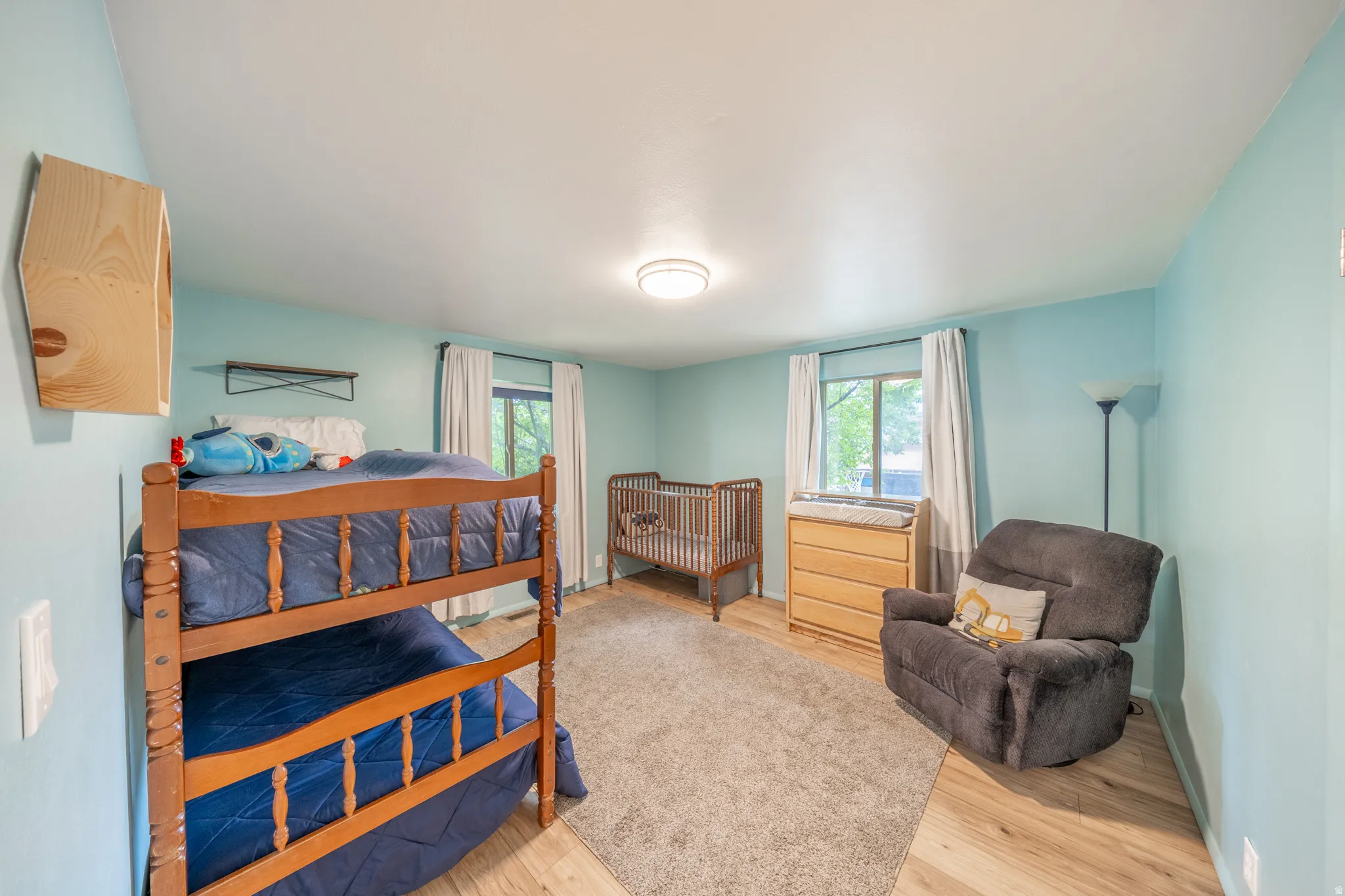 Spacious room featuring light blue walls, wood-finish flooring, and two windows with white curtains