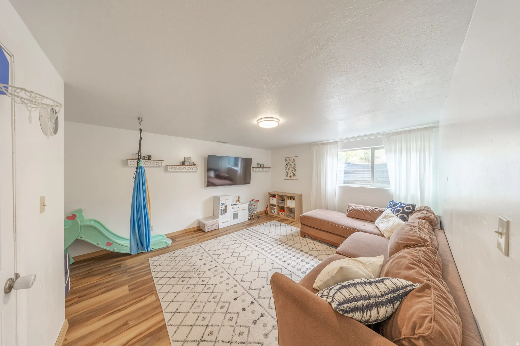 Spacious room featuring wood-finish flooring, recessed lighting, and a window with white sheer curtains