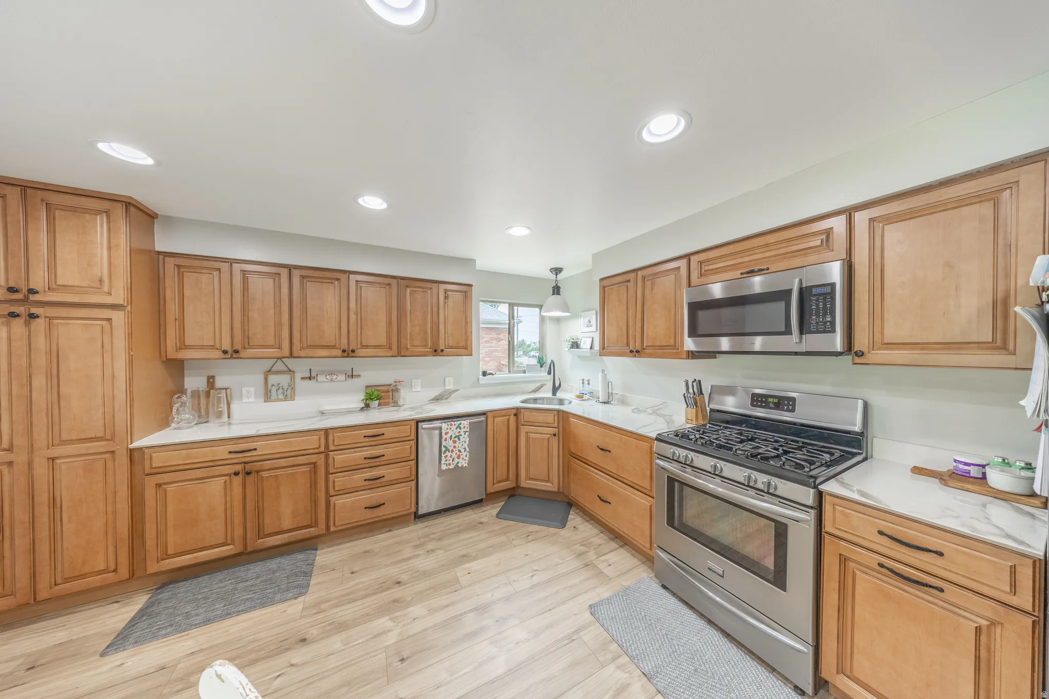 Open-concept kitchen featuring extensive light wood cabinetry, stainless steel appliances, recessed ceiling lighting, light-toned countertops, and wood-finish flooring