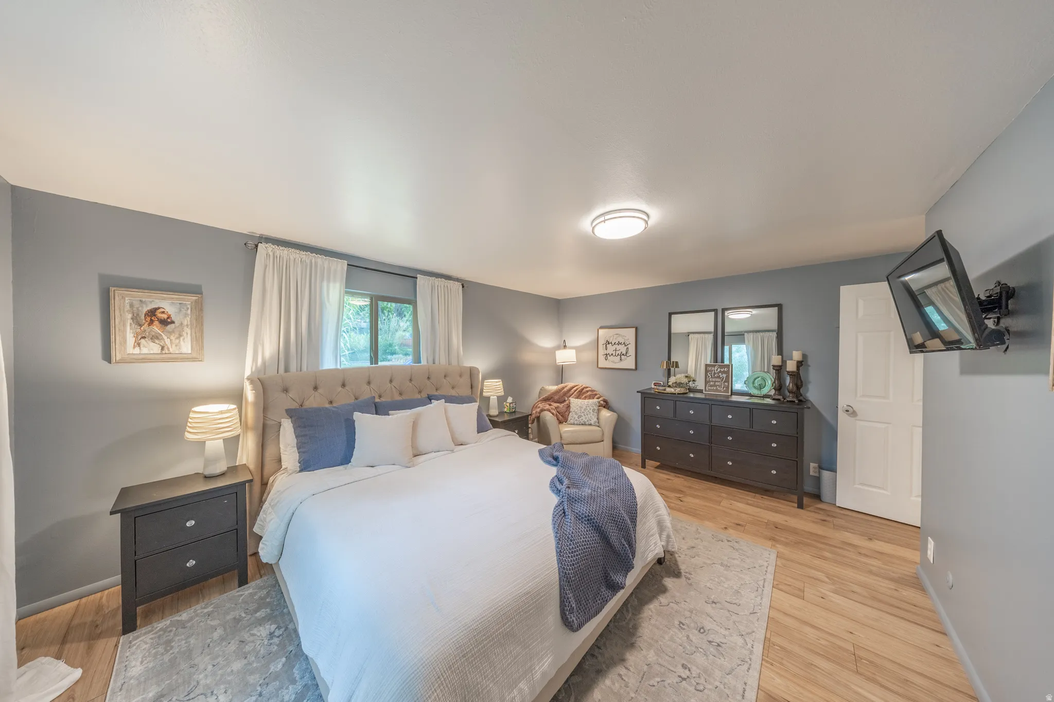Spacious room featuring light wood-finish flooring, light blue walls, and a recessed window with white curtains
