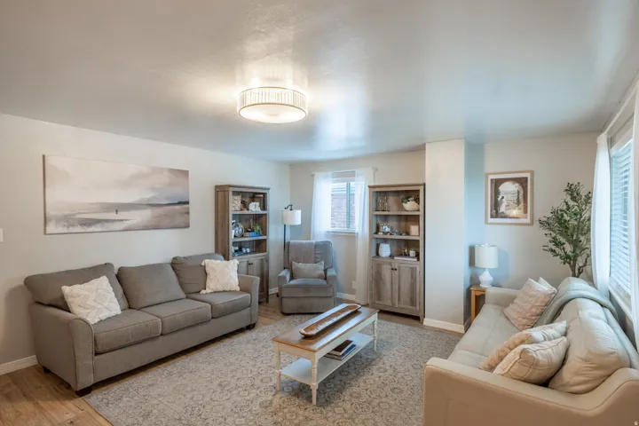 Spacious living area featuring light-toned walls, wood-finish flooring, and a decorative ceiling light fixture
