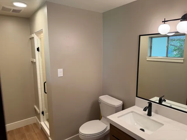 Bathroom featuring a glass-enclosed shower, wood-finish flooring, a contemporary vanity with a white countertop, a rectangular undermount sink, and a black-framed mirror