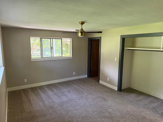 Spacious room featuring neutral carpeting, a gold-finish ceiling fan, and a large window