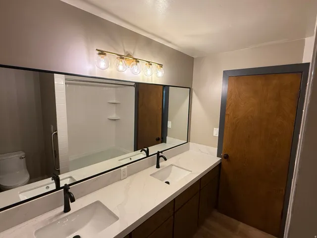 Bathroom featuring a dual vanity with undermount sinks, quartz countertops, matte black faucets, and wood-finish cabinetry