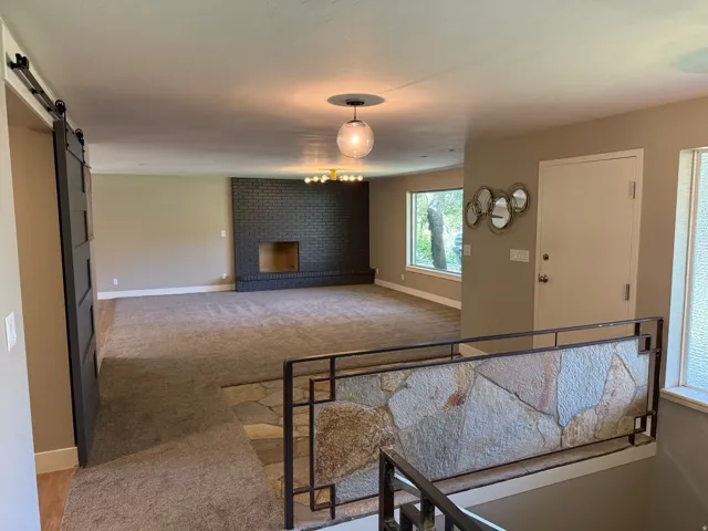 Spacious living area featuring a dark brick fireplace, contemporary brass chandelier, and large windows