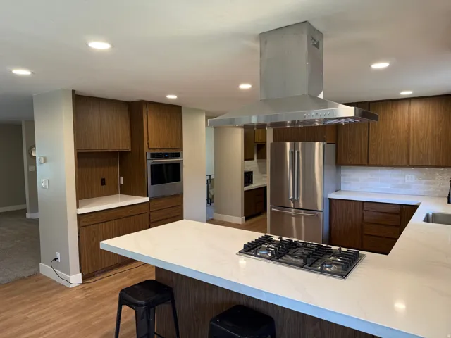 Kitchen featuring an island with a gas cooktop, recessed lighting, wood-finish cabinetry, stainless steel appliances, and light-toned countertops
