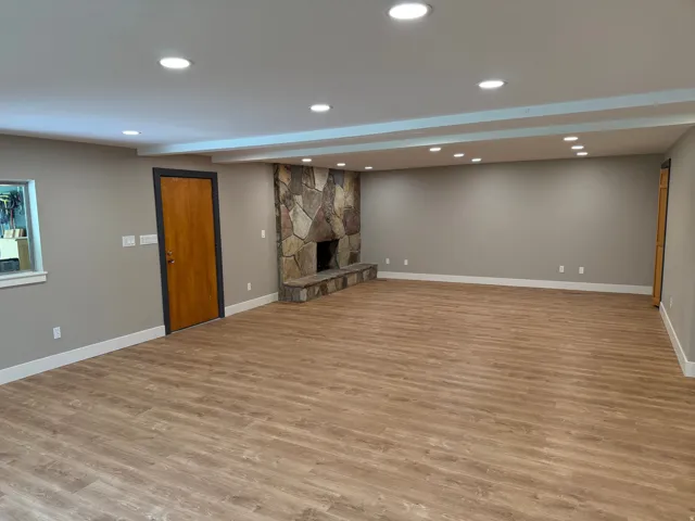 Spacious room featuring a prominent stone fireplace with a raised hearth, wood-finish flooring, and recessed ceiling lighting