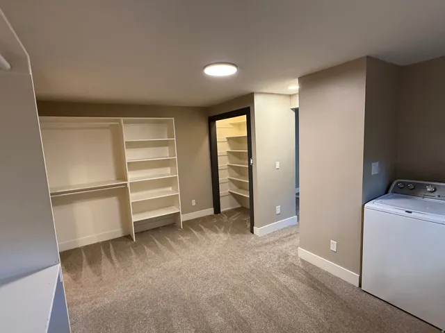 Functional laundry area with a top-load washing machine, built-in shelving, carpet flooring, and recessed lighting