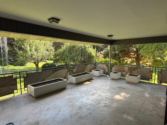 Covered patio with a concrete surface, featuring an open railing design with stone accents, offering expansive outdoor space