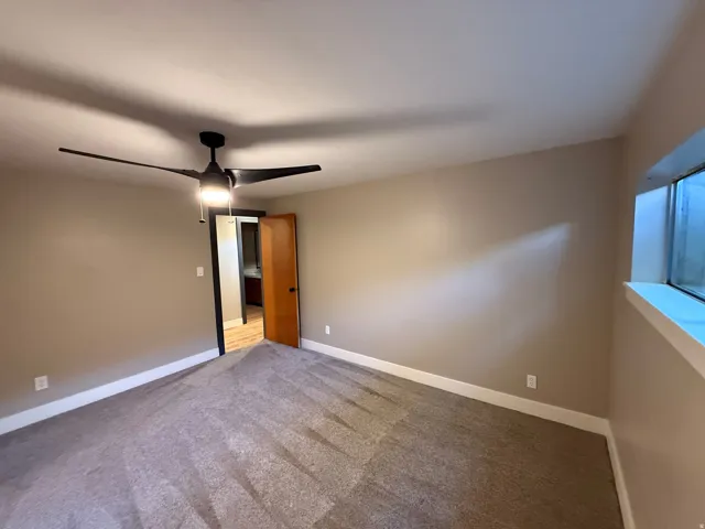 Carpeted room featuring a modern ceiling fan with integrated lighting, a recessed window, and neutral wall tones