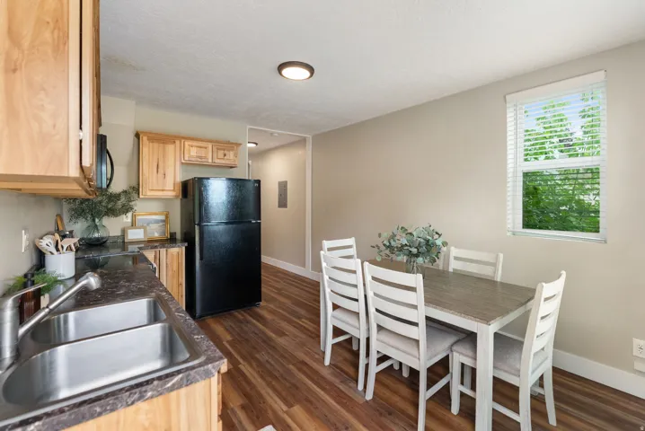 West unit. Kitchen and dining area featuring wood-finish flooring, natural wood cabinetry, a double basin stainless steel sink, black appliances, and a window with horizontal blinds