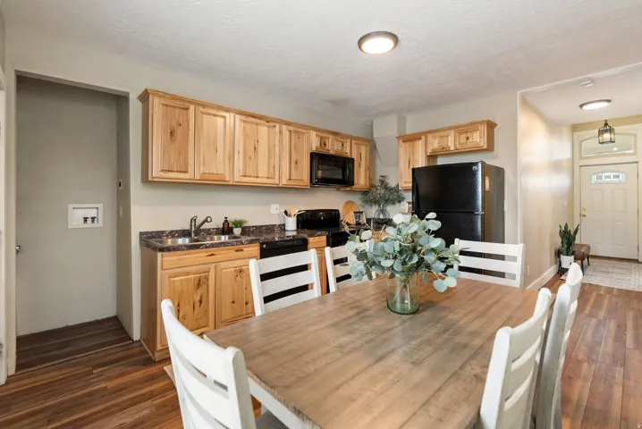 West unit. Open-concept kitchen and dining area featuring natural wood cabinetry, dark countertops, and black appliances