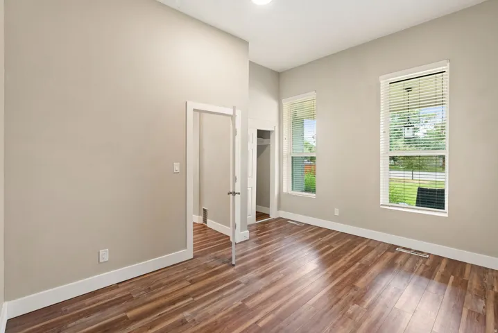 East unit - Bedroom #1. Spacious room featuring vaulted ceilings, wood-finish flooring, two large windows with blinds, a built-in closet, and a neutral wall color