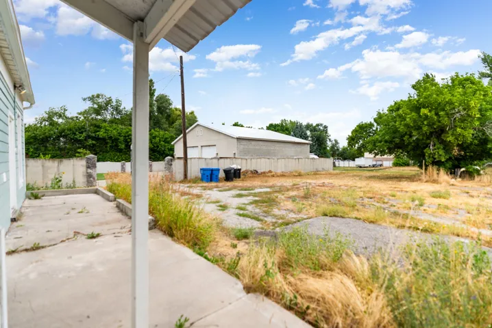 Backyard featuring a concrete patio, mature trees, and a substantial outbuilding with garage doors