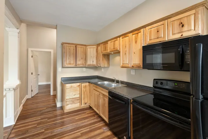 East unit. Kitchen featuring wood-finish flooring, natural wood cabinetry, dark countertops, and black appliances including a microwave, dishwasher, and electric range