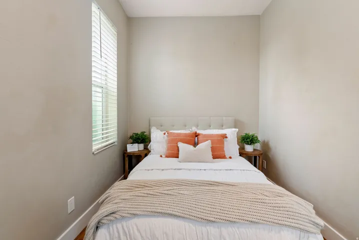 West unit. Bedroom featuring a window with blinds, light-toned walls, and wood-finish flooring